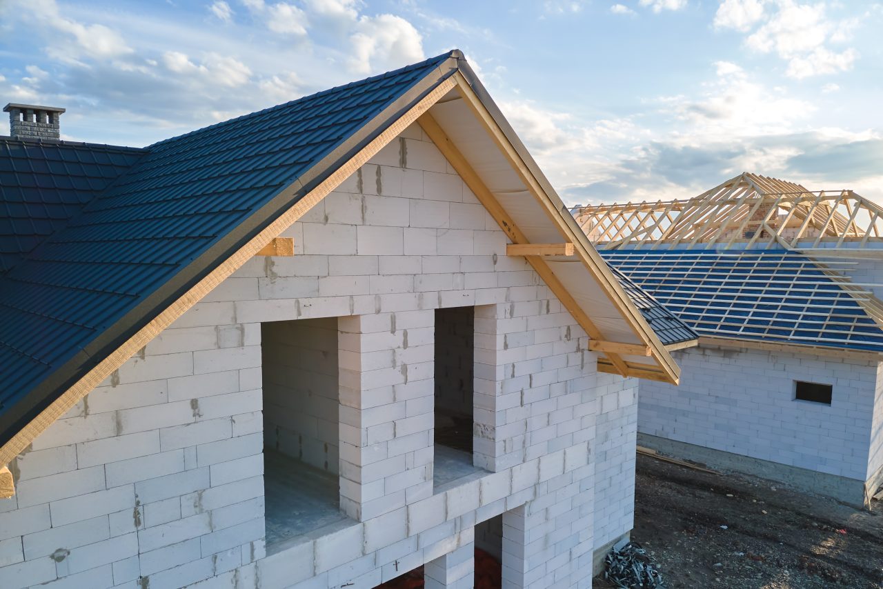 Aerial view of unfinished house with aerated lightweight concrete walls and wooden roof frame covered with metallic tiles under construction.